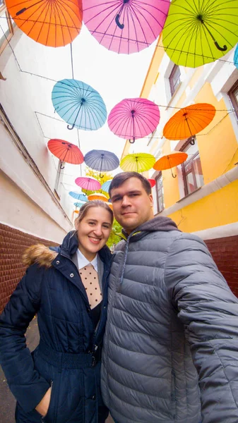 Retrato de feliz sorrindo jovem casal posando contra guarda-chuvas coloridos na instalação de arte de rua — Fotografia de Stock