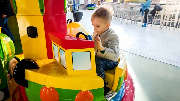 Portriat de menino da criança alegre montando no carrossel colorido com barcos de brinquedo no parque de diversões no shopping — Fotografia de Stock