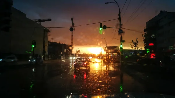 Abstract image through wet car windshield on movng transport and autuomobiles in rain at sunset rays — Stock Photo, Image