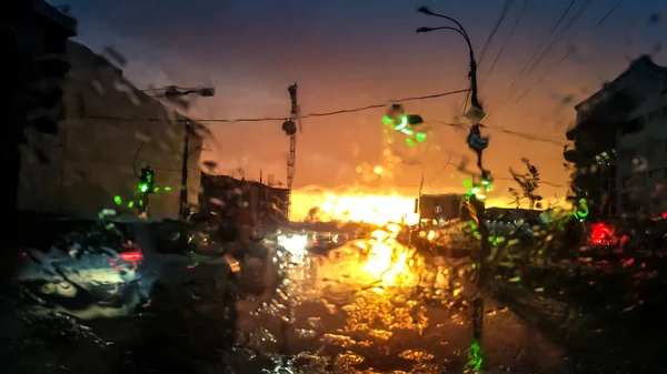 Abstraktes Bild durch nasse Autoscheibe auf fahrendem Transport und Automobile bei Regen bei Sonnenuntergang — Stockfoto