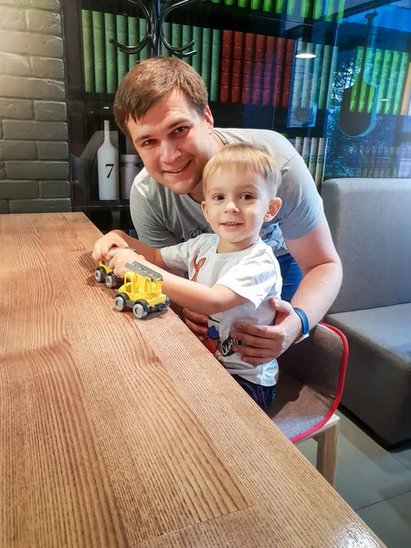 Retrato de niño feliz jugando con su padre con juguetes de plástico mientras está sentado detrás del mostrador en la cafetería —  Fotos de Stock