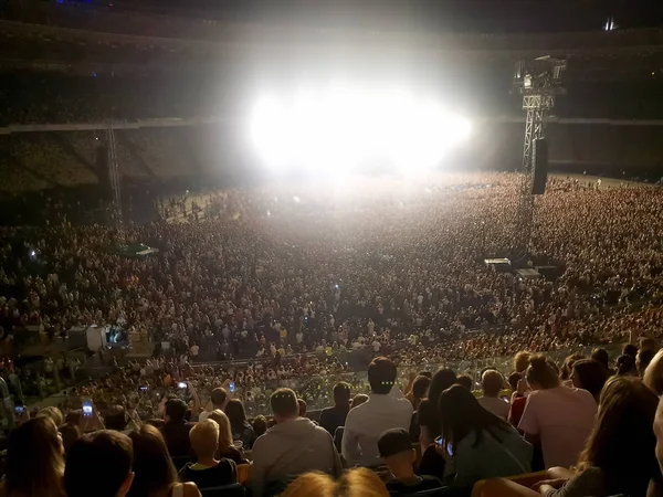 Gran multitud de fans sentados en los tribunos del estadio y escuchando conciertos de música rock por la noche. Luz brillante y rayos láser que iluminan la escena del espectáculo —  Fotos de Stock