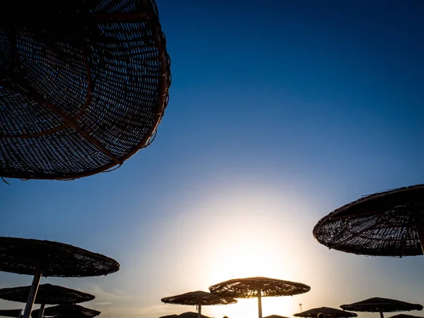 Slihouette imagen de sombrillas de protección solar hechas de paja en la playa del mar contra el cielo azul brillante — Foto de Stock