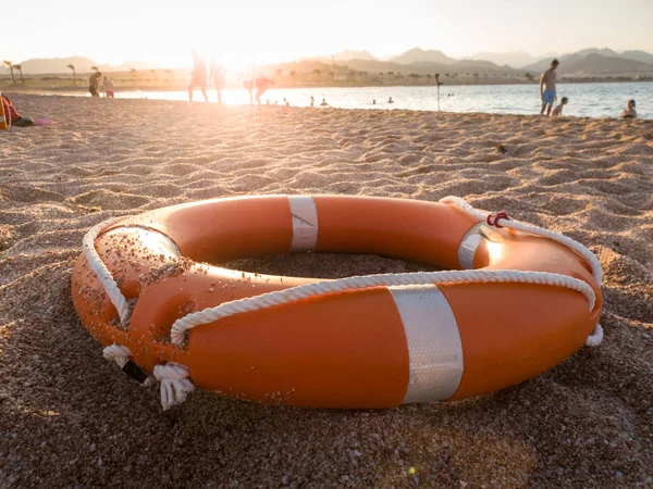 Foto de primer plano del anillo de plástico naranja para salvar a las personas que se ahogan en el mar tumbadas en la playa —  Fotos de Stock