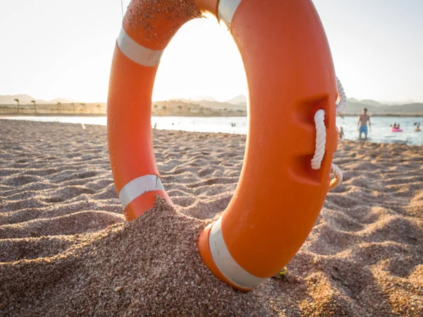 Foto de primer plano del anillo de plástico naranja para salvar a las personas que se ahogan en el mar tumbadas en la playa — Foto de Stock