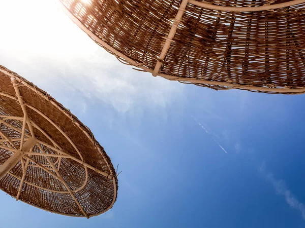 Slihouette bild av solskydd parasoller gjorda av halm på havet stranden mot klarblå himmel — Stockfoto