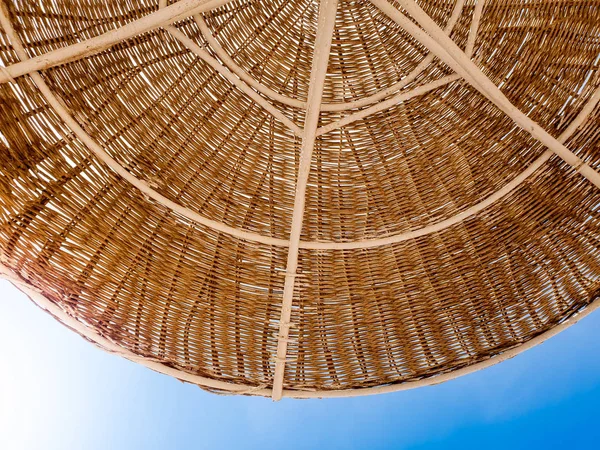 Nahaufnahme eines Teils eines Strohschirms, der vor Sonne am Strand vor blauem Himmel schützt. Perfektes Image für den Sommerurlaub oder Urlaub. Platz für Ihren Text. Kopierraum. — Stockfoto