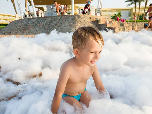 Портрет милого малыша, играющего и веселящегося с большим количеством мыльной пены на пляжной дискотеке — стоковое фото