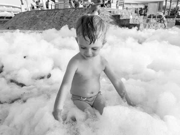 Czarno-biały portret adorable malucha chłopiec gra z dużą ilością mydła po morzu plaży Disco party — Zdjęcie stockowe