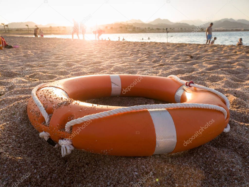 Closeup photo of orange plastic ring for saving drowning people on the sea lying on beach