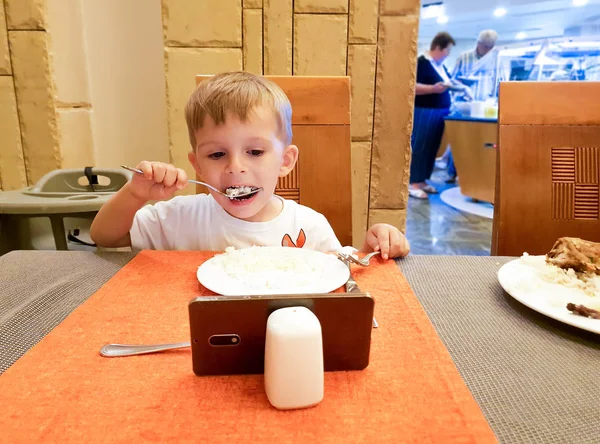 Restoran veya kafede yemek yerken akıllı telefonda çizgi film izleyen küçük çocuğun portresi — Stok fotoğraf