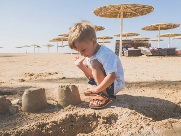 Stonowany obraz uroczego chłopca malucha siedzącego na piaszczystej plaży i budynku zamku z mokrego piasku — Zdjęcie stockowe