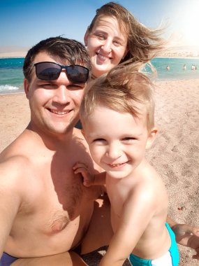 Güneşli rüzgarlı bir günde deniz plajında mutlu gülümseyen neşeli ailenin selfie portresi. Aile rahatlatıcı ve yaz tatili tatili sırasında iyi vakit geçirmek.