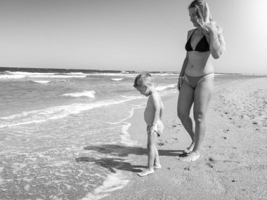 Sahilde sıcak deniz dalgaları nda duran küçük oğlu ile güzel genç anne siyah beyaz görüntü. Aile rahatlatıcı ve yaz tatili tatili sırasında iyi vakit geçirmek.