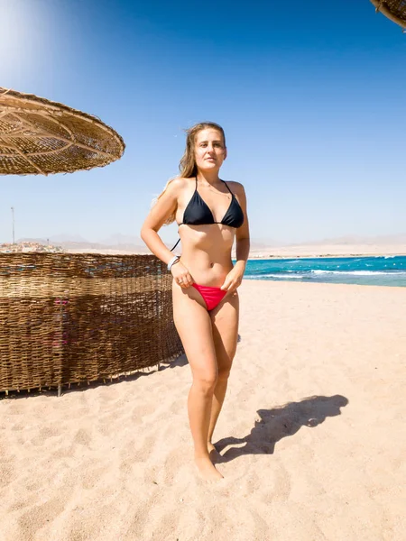 Vacker ung kvinna med långt hår och perfekt kropp stående på sandstranden havet vid titta i kameran. Flicka avkopplande och ha god tid under sommarlovet semester. — Stockfoto