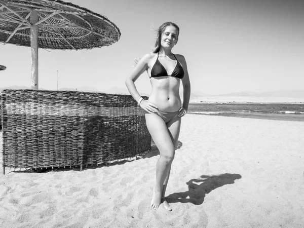 Imaginea alb-negru a unei tinere sexy în bikini pozând pe plaja de nisip la o zi însorită strălucitoare. Fata relaxare și având timp bun în timpul vacanței de vară . — Fotografie, imagine de stoc