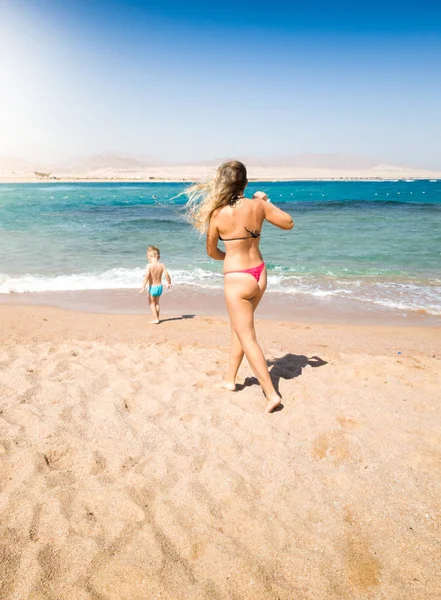 Imagem de uma jovem mãe correndo para seu filhinho andando no mar. Cuidar dos pais evitando a situação de perigo durante as férias na praia . — Fotografia de Stock