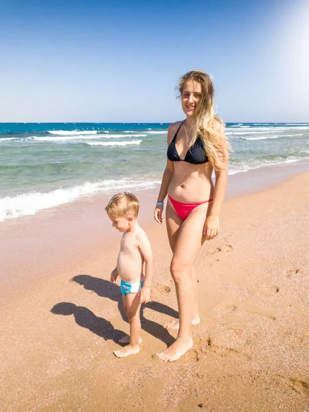 Bild einer glücklichen jungen Mutter, die mit ihrem kleinen Sohn am schönen Meeresstrand spazieren geht. Familie entspannen und Spaß haben im Sommerurlaub. — Stockfoto