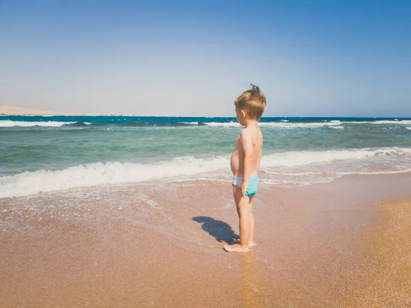 Stonowany obraz 3 lat chłopiec maluch stoi na plaży morskiej i patrząc na horyzoncie. Dziecko relaksujące i dobrze się bawią podczas letnich wakacji. — Zdjęcie stockowe