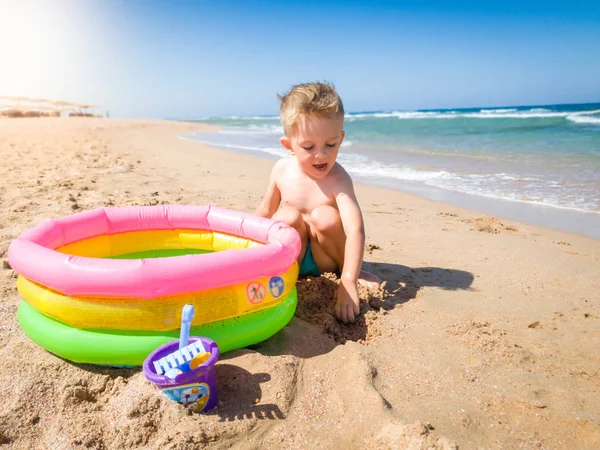 Szczęśliwy wesoły toodler chłopiec digigng piasku na plaży i grając z nadmuchiwanym basenem. Dziecko relaksujące i dobrze się bawią podczas letnich wakacji. — Zdjęcie stockowe