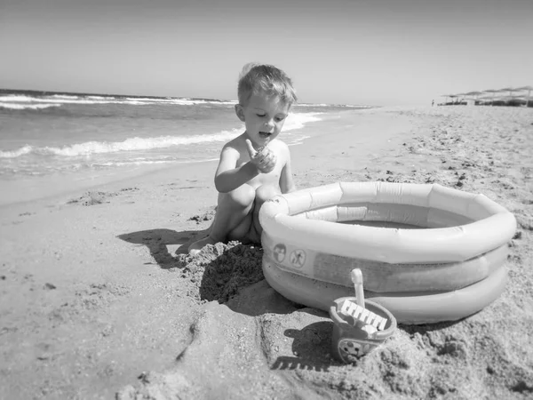 Czarno-białe zdjęcie chłopca bawiącego się na plaży morskiej z nadmuchiwanym basenem. Relaks dla dzieci i miło spędzony czas podczas wakacji letnich. — Zdjęcie stockowe