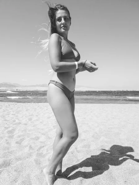 Portrait noir et blanc d'une jeune femme souriante aux cheveux longs posant contre une belle plage de sable et des vagues de mer — Photo