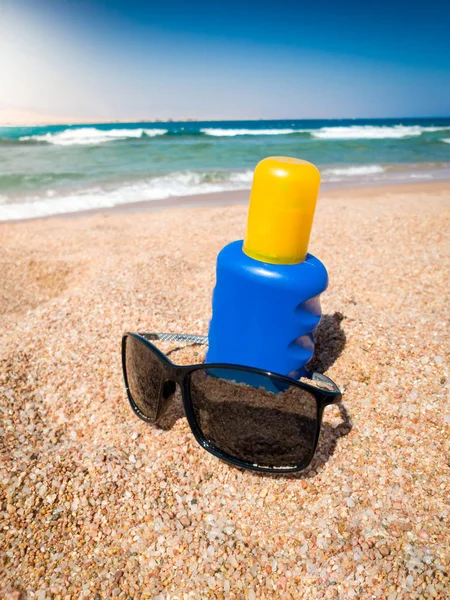Imagen de cerca de gafas de sol y crema solar en la playa de arena de mar. Imagen perfecta para ilustrar vacaciones de verano . —  Fotos de Stock