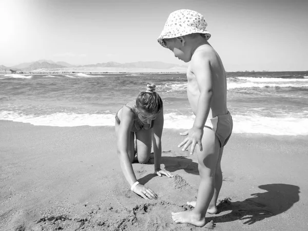 Czarno-biały obraz małego chłopca malucha bawiąc się z młodą matką na plaży morskiej. Rodzinny relaks i dobry czas podczas letnich wakacji. — Zdjęcie stockowe