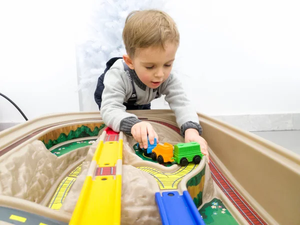 Ritratto di adorabile bambino che gioca con treni giocattolo di plastica colorati — Foto Stock