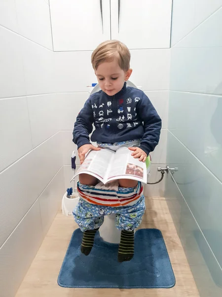 화장실에 앉아 잡지를 읽는 작은 3 살 짜리 유아 소년의 재미있는 이미지 — 스톡 사진