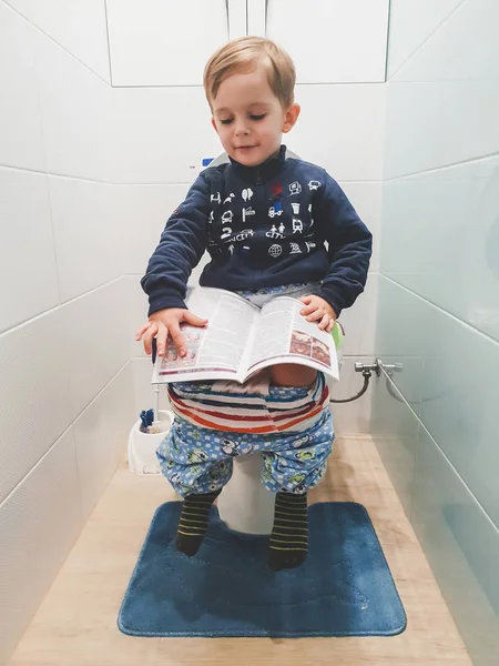 Toned portrait of smart little boy stting on the toilet and reading  magizines Stock Photo by ©Kryzhov 268740956