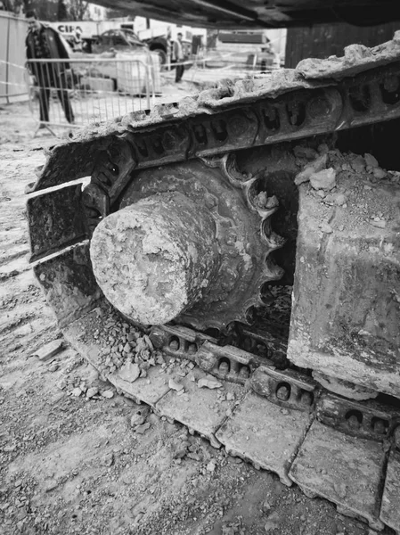 Крупный план черно-белого изображения металлических рельсов экскаватора и шестеренок, покрытых грязью на строительной площадке — стоковое фото