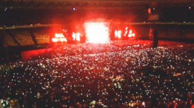 Stadyum koltuklarında oturan ve geceleri rock konseri dinleyen taraftarların odak görüntüsü.