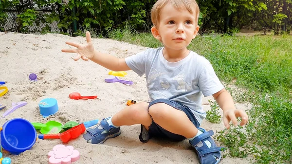 Портрет маленького мальчика, играющего с игрушками и песком на площадке — стоковое фото