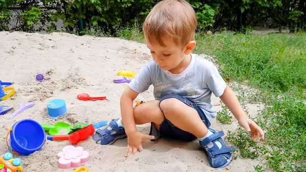Retrato de un niño jugando con juguetes y cavando arena en un arenero en el parque — Foto de Stock