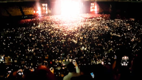 Out of focus image of big crowd of fans sitting on stadium seats watching and listening rock concert at night. — Stock Photo, Image