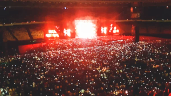 Stadyum koltuklarında oturan ve geceleri rock konseri dinleyen taraftarların odak görüntüsü.