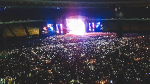 Foto desenfocada del gran estadio lleno de fans en el concierto de música rock. Fondo perfecto para ilustrar fiestas, discotecas o festivales de música —  Fotos de Stock
