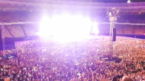 Z ohnisku obrazu velkého davu fanoušků sedících na sedadlech na stadionu pozorují a naslouchají rockový koncert v noci.. — Stock fotografie