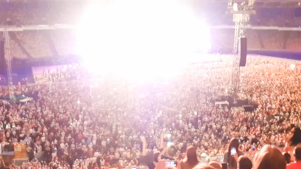 Photo déconcentrée de personnes écoutant et regardant un grand concert de rock sur un festival de musique au grand stade. Une foule de fans assis sur les tribunes la nuit. Scène éclairée avec faisceaux lumineux et lasers — Photo