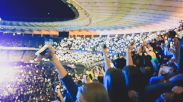 Defocused image of big crowd of fans making image on smartphones and holding flashlights on the rock concert.