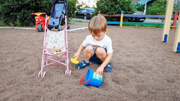 Söt 3 år gammal liten pojke som leker på barnens lekplats i parken. Småbarns grävning sand med skyfflar — Stockfoto