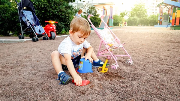 Cute 3 years old little boy playing on the children playground in park. Toddler digging sand with shovels — Stock Photo, Image
