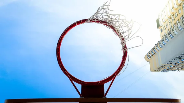 Nahaufnahme eines Basketballrings mit Netz vor blauem Himmel und hohem Gebäude im Wohnviertel der Stadt — Stockfoto