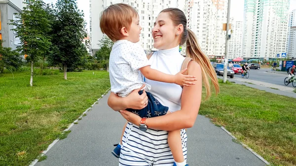 Retrato de una joven feliz y sonriente abrazando a su hijo pequeño y caminando por la calle de la ciudad —  Fotos de Stock