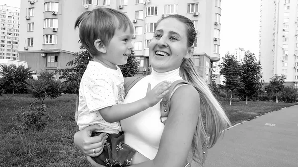 Zwart-wit portret van gelukkig glimlachende jonge moeder knuffelen haar kind zoon wandelen op City Street — Stockfoto