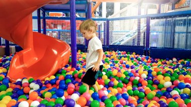 Photo of little boy playing in the pool full of colroful plastic balls. Toddler having fun on playground in shopping mall clipart