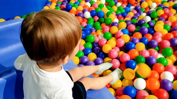 小さなカラフルなプラスティックボールの多くと遊び場で遊んで楽しんでいる3歳の幼児の男の子の画像。ショッピングモールで遊園地を楽しむ子供 — ストック写真
