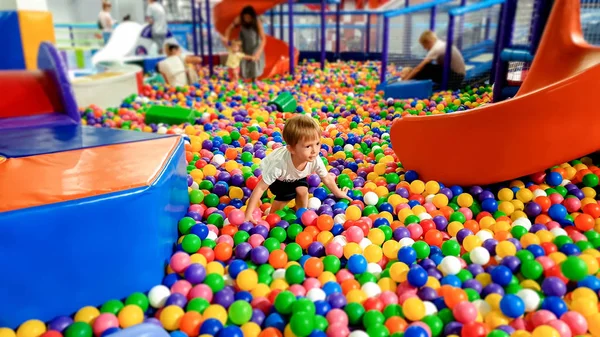 Menino pequeno andando e escalando sobre lotes de bola de plástico colorido no playground no shopping — Fotografia de Stock
