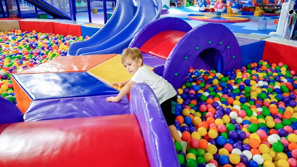 小さな幼児の男の子が歩いて、ショッピングモールの遊び場でカラフルなプラスチックボールの多くを登る — ストック写真